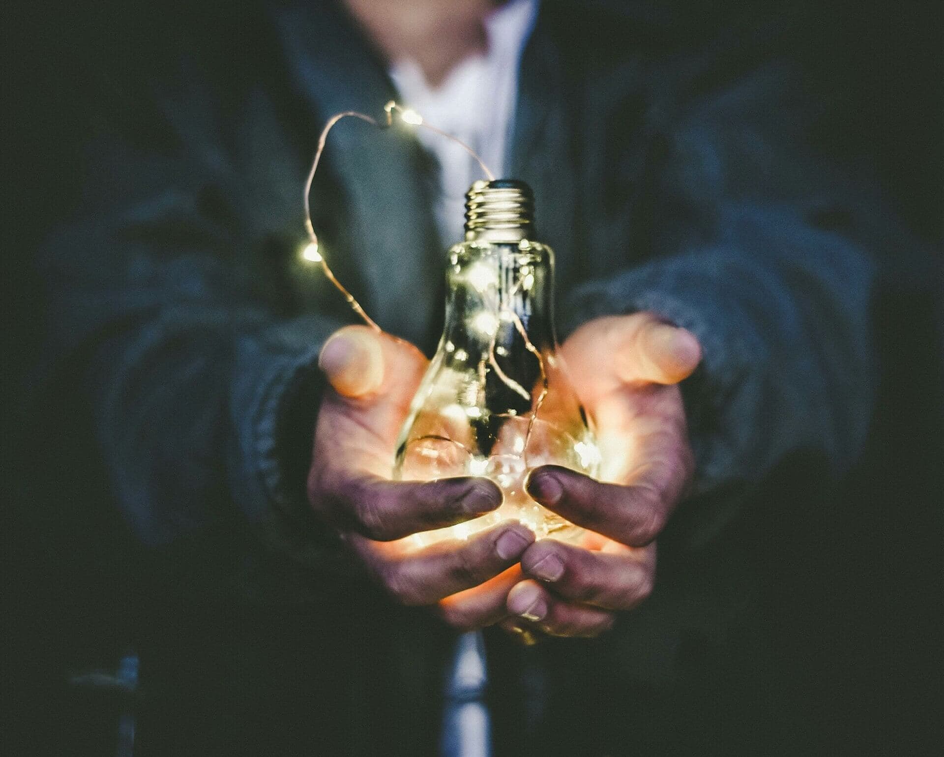 A glowing light bulb held in open hands, symbolizing innovative solutions